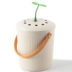 a white container with a green plant sticking out of it's side and a wooden handle