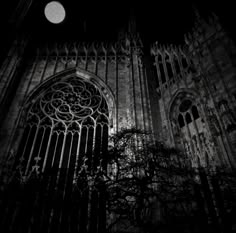 an old gothic cathedral lit up at night with the moon in the sky behind it