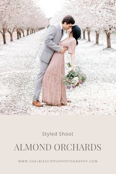 a man and woman standing next to each other in front of trees with white flowers