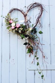 a heart shaped wreath with flowers and greenery hanging on a white wooden wall in front of a door