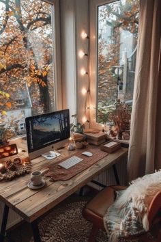 a desk with a computer on it in front of a window filled with fall leaves