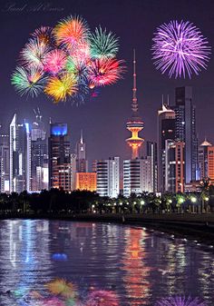 fireworks are lit up in the night sky over a cityscape and water with buildings