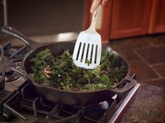 a spatula is being used to stir greens in a skillet on the stove