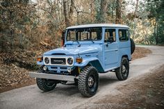 a light blue jeep is parked on the side of a road in front of some trees