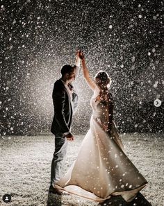 a bride and groom dancing in the snow at their winter wedding reception, with falling snow all around them