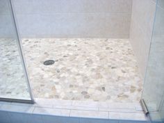 a walk in shower sitting next to a white tiled wall and floor covered in pebbles