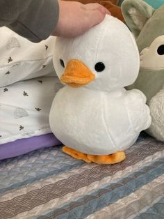 two stuffed animals sitting on top of a bed next to a person's hand