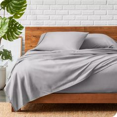 a bed with grey sheets and pillows on top of it next to a potted plant