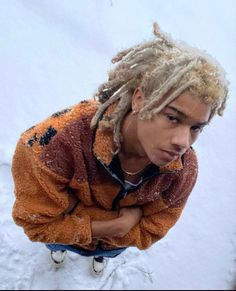 a man with dreadlocks standing in the snow wearing an orange and brown jacket