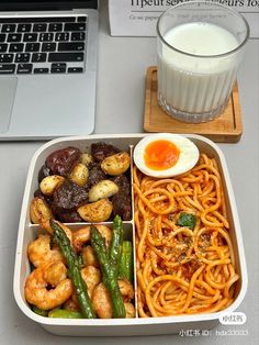 a lunch box with pasta, asparagus, and shrimp next to a glass of milk