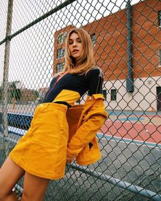 a woman leaning against a fence with her hands on her hips and looking at the camera