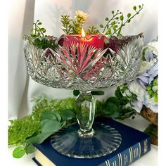 a glass bowl filled with flowers and an apple sitting on top of a blue book