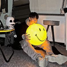 a young man holding a yellow smiley face ball in front of his face while sitting on the floor