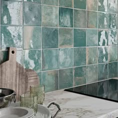 a kitchen with green tiles on the wall and silver dishes sitting on the counter top