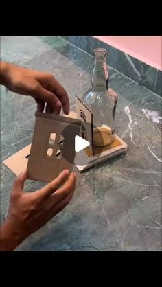 two hands are opening up a cardboard box with a bottle on the table next to it