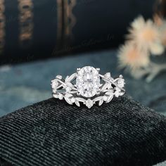 a diamond ring sitting on top of a black piece of cloth with flowers in the background