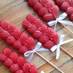 red heart shaped lollipops with white bows on them sitting on a wooden table