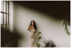 a woman leaning against a wall with her hand on her head and looking at the camera