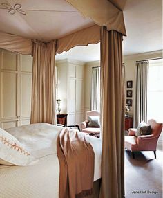 a bedroom with four poster bed, pink chair and beige drapes on the ceiling