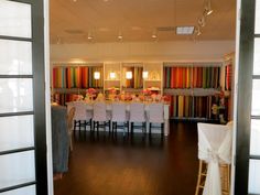 a room filled with lots of white chairs and tables covered in cloths on top of hard wood flooring