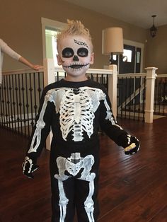 a young boy in a skeleton costume standing on a wooden floor with his hands out