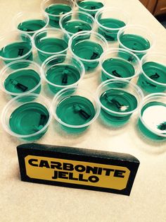 there are many plastic cups on the table with green liquid in them and a sign that says carbonite jello