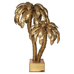 a brass palm tree sculpture on a wooden base with gold foiled leaves, in front of a white background