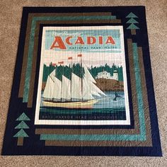 a quilted wall hanging with a sailboat on the water and pine trees in the background