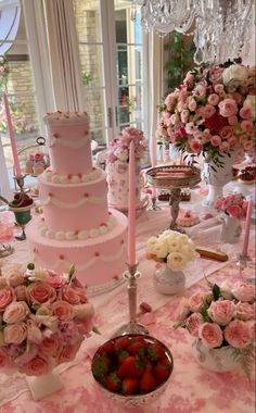 a table topped with a pink wedding cake and lots of flowers next to a bowl of strawberries