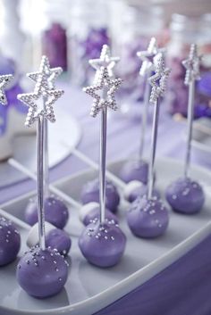 purple cake pops with silver stars on them are sitting on a tray at a party