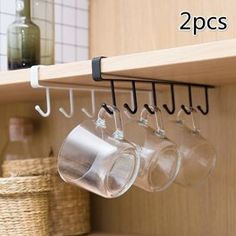 three wine glasses hanging from a wooden shelf in a kitchen with hooks and cups on it