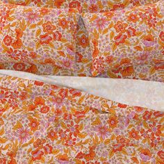 an orange and pink flowered bed spread with two pillows on top of each other