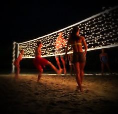 some people are playing volleyball on the beach at night with christmas lights in the background