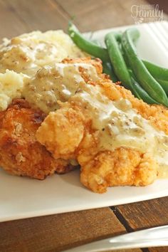 chicken fried chicken with homemade country gravy on a white plate next to green beans