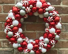 a red and white christmas ornament wreath on the side of a brick wall