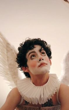 a woman with white makeup and angel wings on her face looking up at the sky