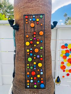 an outdoor sculpture made out of palm tree with colorful circles and dots on the bark