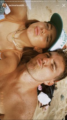 a man and woman are laying on the beach with their heads close to each other