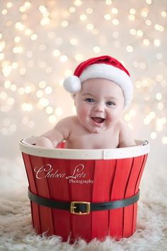 a baby wearing a santa hat sitting in a red bucket with white lights behind it