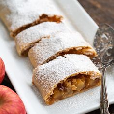 a white plate topped with apple turnovers covered in powdered sugar next to an apple