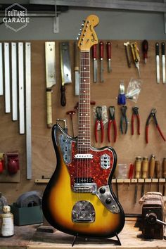 a guitar sitting on top of a wooden table in a room filled with work tools