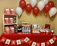 a red table topped with lots of balloons and desserts next to a shelf filled with drinks