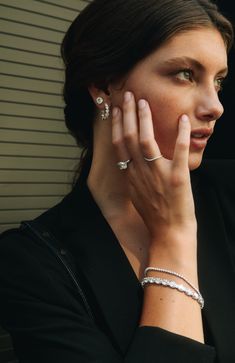 a woman in black jacket holding her hand up to her face with two diamond bracelets on