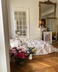 a bed with white sheets and pink flowers on the floor in front of a mirror