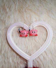 two pink pig earrings are hanging from a white heart shaped hook - on earring