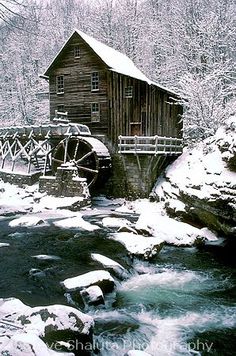 an old mill in winter with snow on the ground and water running under it,