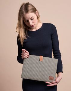 a woman in a black dress is holding a brown and white striped bag with leather handles