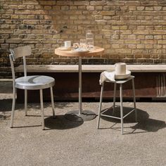 two chairs and a table in front of a brick wall, one with a cup on it