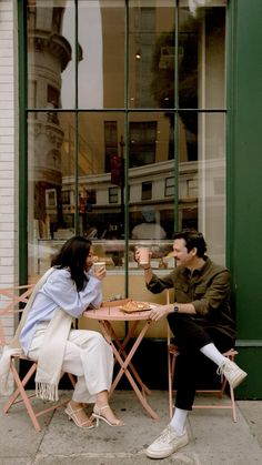 a man and woman sitting at an outdoor table eating pizza, drinking tea or coffee