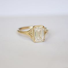 an emerald cut diamond set in a yellow gold ring on a white surface with no background